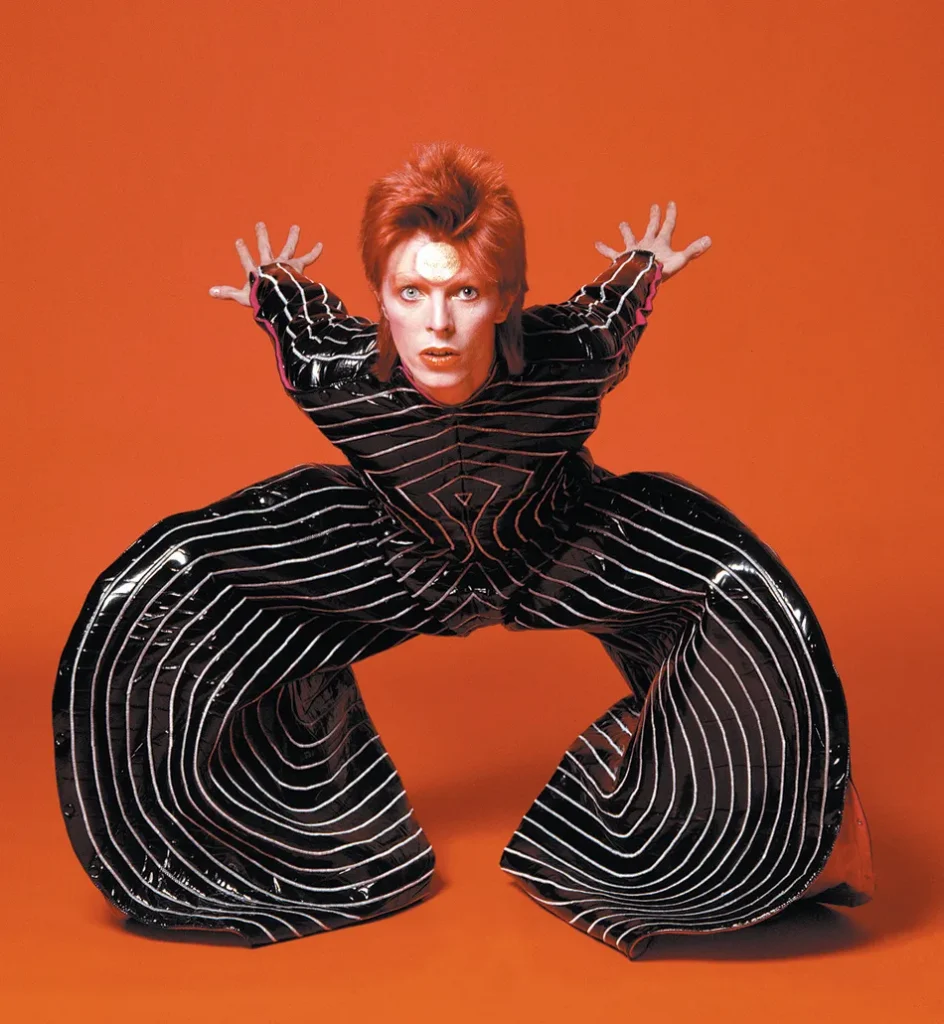 David Bowie con su conjunto negro de vinilo con rayas blancas, diseñado por Kansai Yamamoto.