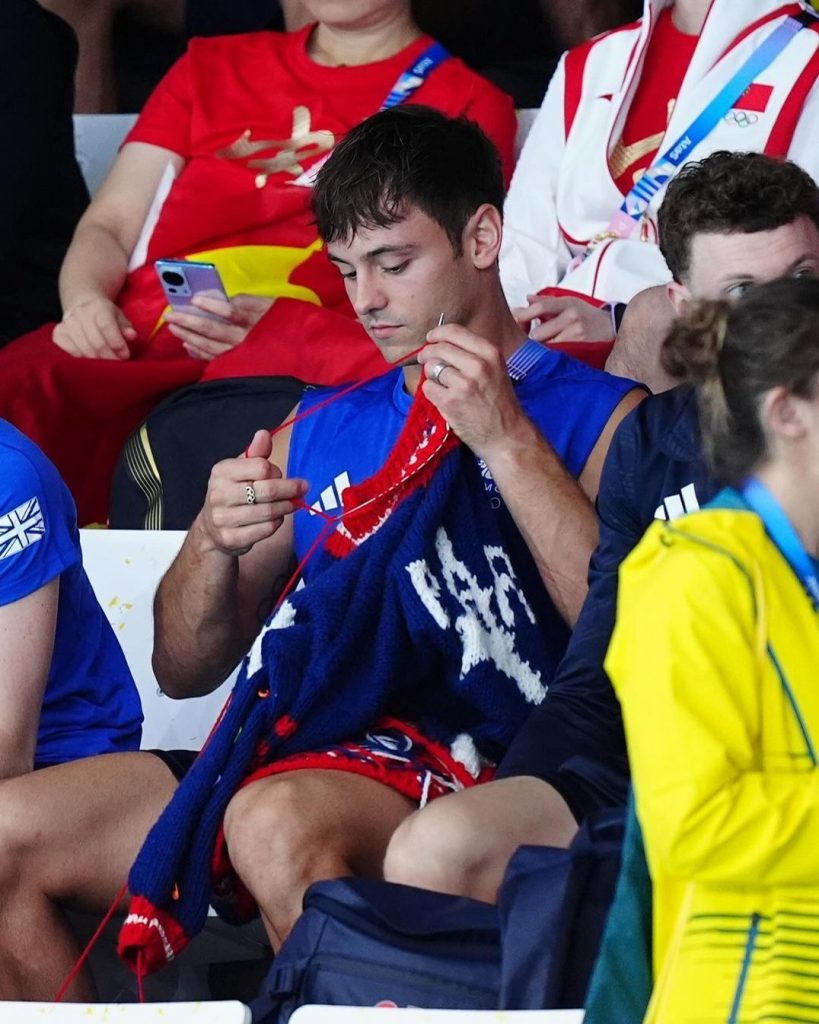 Tom Daley teje en las gradas, junto a la piscina del Centro Acuático de París 2024. 